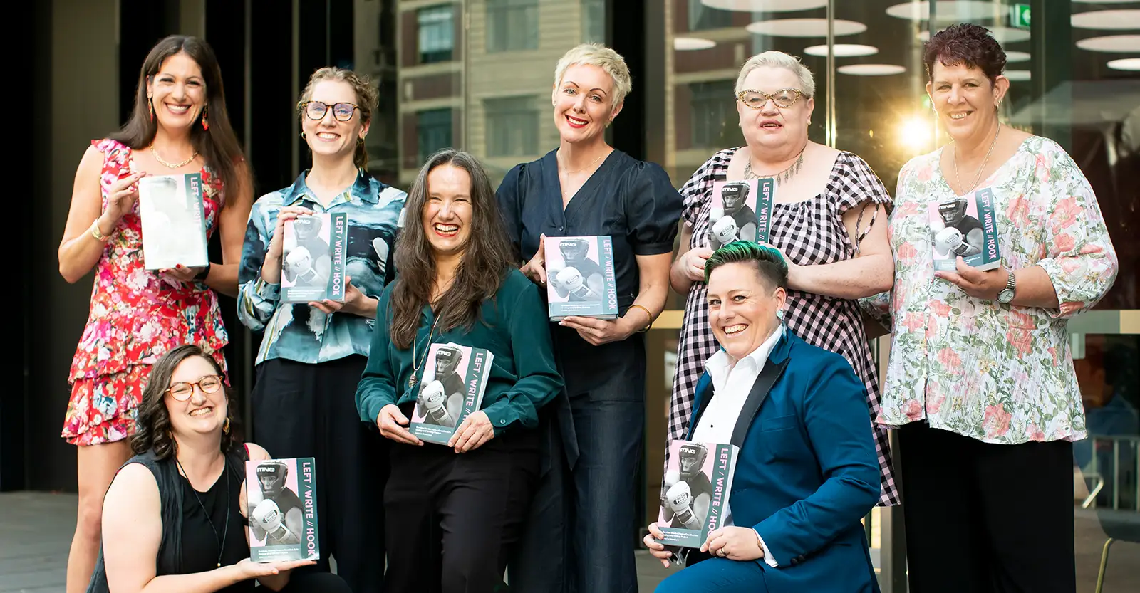 A group of eight participants from the Left Write Hook program, holding up copies of the book and lookign proud and happy.