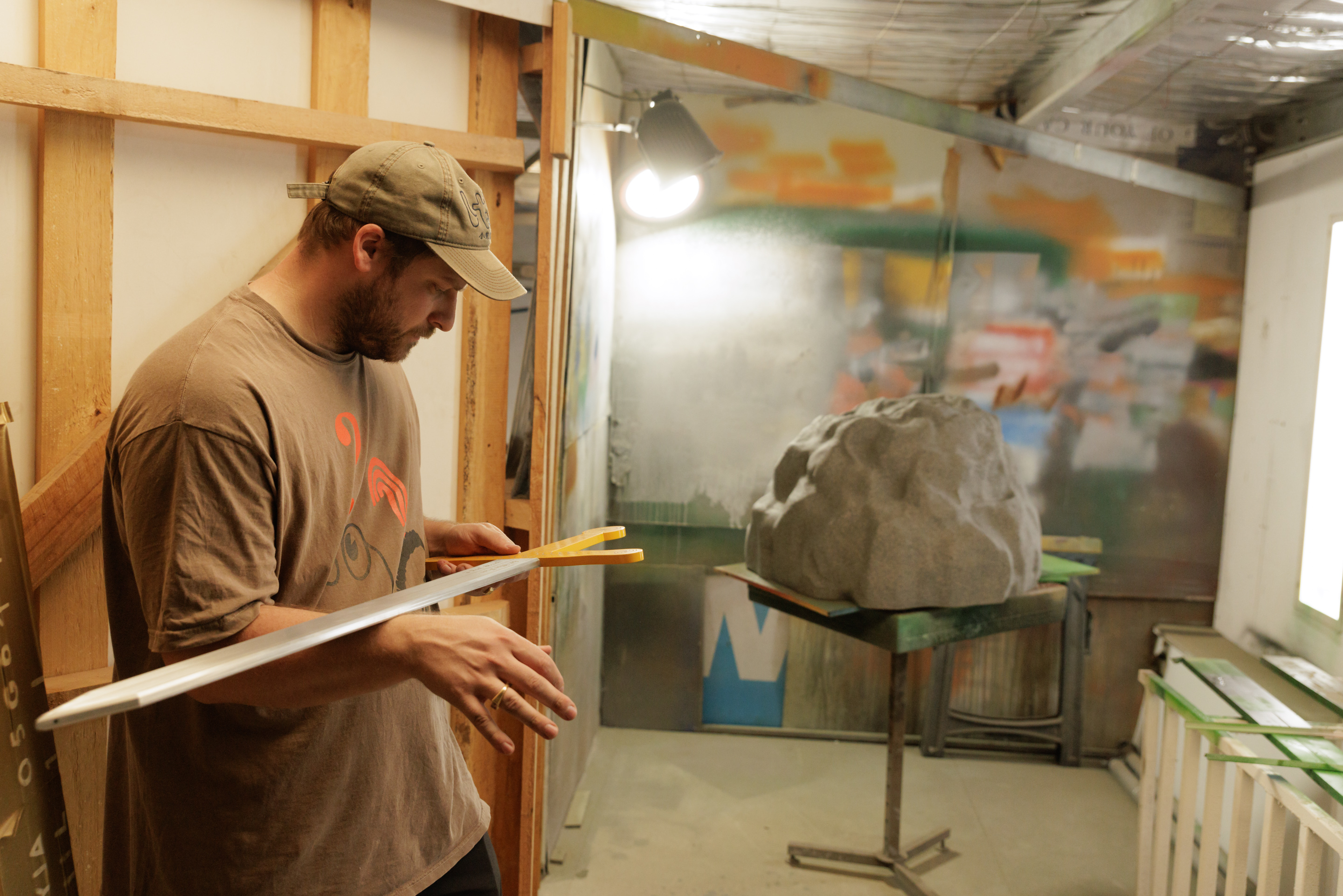 Tim Meakins stands against a theatre flat, balancing a painted wooden sword on his wrist. In the background is a table with a mock stone on it.