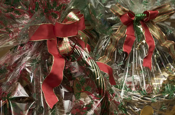 Gift baskets wrapped in a large amount of cellophane with Christmas-themed prints on it.