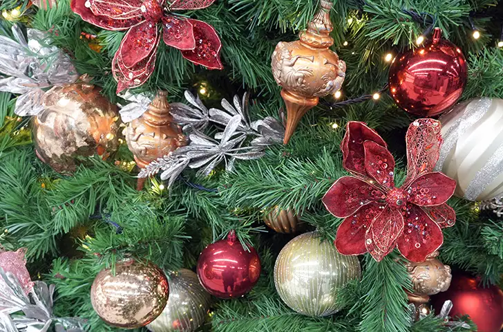 A close up of an artificial Christmas tree with ornate moulded plastic finials, round baubles and textile poinsettia blooms on it.