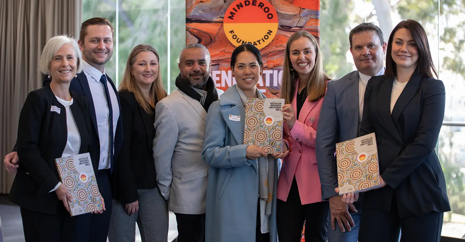 A group of men and women, most of them indigenous, pose for the camera, three of them holding copies of the Indigenous Employment Index.