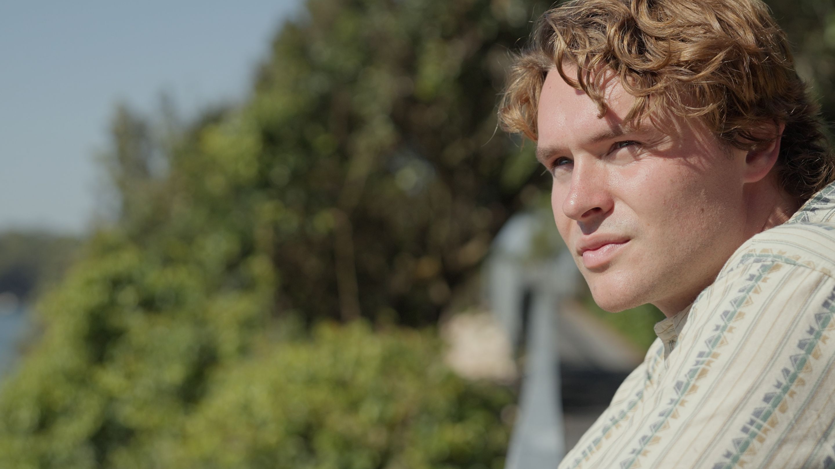 Kal Glanznig, filmmaker and ocean advocate, is pictured looking at at sea. He is surrounded by trees.