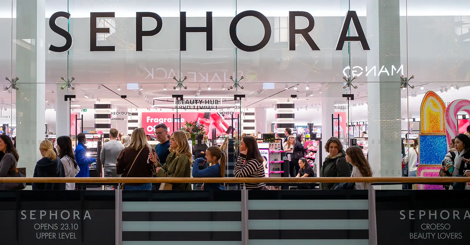 A long short of people queued up along the front of a Sephora store that is brightly lit.