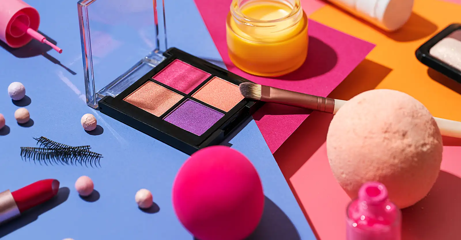 This collection of beauty products is very brightly coloured, with the products in yellow, pink and purple colours, lying on top of blue, pink, peach and orange coloured card.